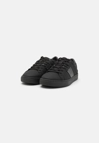 Sneakers neri con finitura opaca liscia, caratterizzati da una toppa testurizzata a contrasto sul lato, punta rotonda e design con lacci.