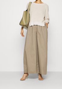Pull en maille beige avec un large col rond, associé à un pantalon ample couleur beige sable. Sac à main vert avec une finition lisse et des accents de quincaillerie discrets.