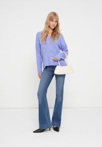 Pulover tricotat de culoare mov deschis, cu maneci lungi, asortat cu blugi evazați albaștri. Accesoriile includ o geantă mică albă și pantofi cu toc ascuțit negri.