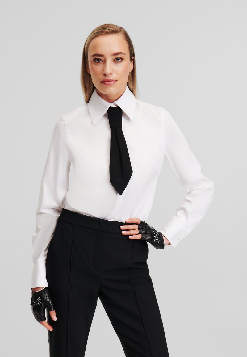 White button-up shirt with a large collar, black tie, and high-waisted black trousers. Black fingerless gloves accentuate the outfit.