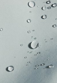 Vanddråber på en lys blå, struktureret stofoverflade, der viser forskellige størrelser og former og fremhæver materialets vandafvisende egenskaber.