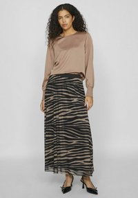 Hnedý saténový top s dlhým rukávom skombinovaný s čiernou a béžovou zebra vzorovanou skladanou maxi sukňou. Modelka má na sebe čierne špicaté topánky.