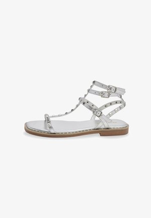 Sandales argentées à lanières avec plusieurs boucles ajustables, finition métallique lisse, semelle plate et clous décoratifs sur les lanières.