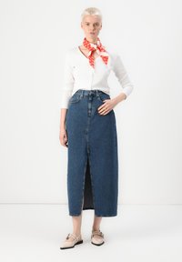 Denim maxiskjørt med frontspalte, blå farge, høy midje-design og lett stoff. Kombinert med en hvit langermet topp og skjerf.