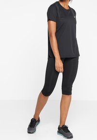 Camiseta deportiva negra de manga corta combinada con leggings capri negros. Presenta un diseño elegante y una tela ligera. Zapatillas de correr negras completan el look.