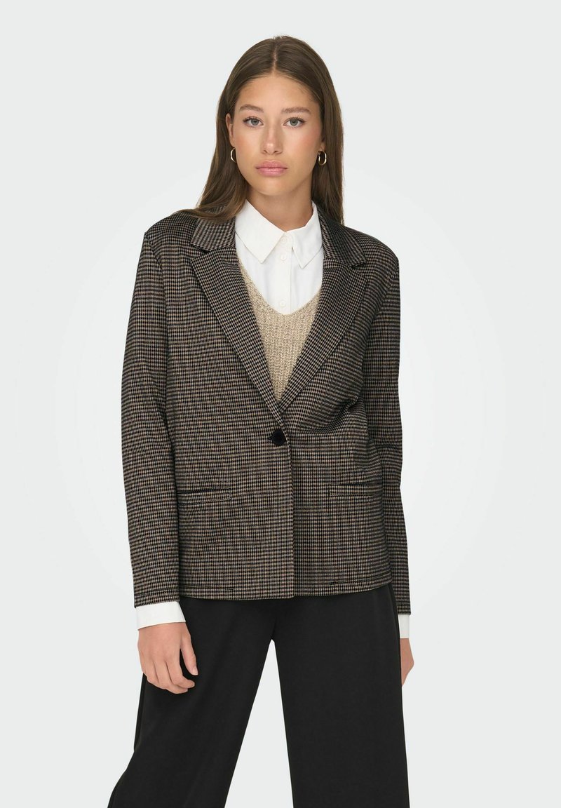 Black and brown checkered blazer with a single button, tailored fit, and flapped pockets, worn over a white shirt and beige knit sweater.