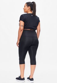 Zwart cropped sporttop met korte mouwen en zwarte hooggesneden leggings, gecombineerd met donkere sneakers. Gladde, rekbare stof.