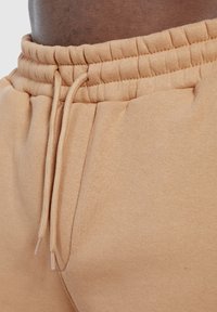 Sweatpants aus einer Baumwollmischung in einem hellen Beige. Der Bund hat eine elastische Raffung mit einem Kordelzug, und die seitlichen Taschen sind sichtbar.