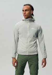 Lichtgrijze, lichtgewicht hoodie met een rits aan de voorkant en elastische mouwen. Gepaard met groene cargobroek, voorzien van zakken en een casual pasvorm.