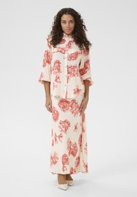 Two-piece floral outfit featuring a cream blouse with red flower print and matching long skirt. Soft fabric with a relaxed fit and buttons.
