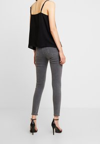 Černý top bez rukávů s nastavitelnými ramínky, v kombinaci se slim-fit šedými džíny a černými sandály na kotníku. Jednoduchý design, hladká textura.