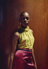 Haut halter en dentelle jaune avec un col à volants, assorti à une jupe en satin lisse bordeaux taille haute dotée d'une ceinture noire. Fond en bois.