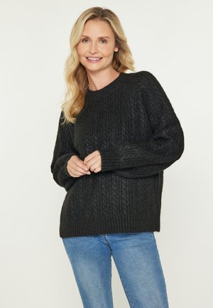 Donker gebreid sweater met een geribbelde textuur, ronde halslijn en lange mouwen. Gecombineerd met lichtblauwe denim jeans.