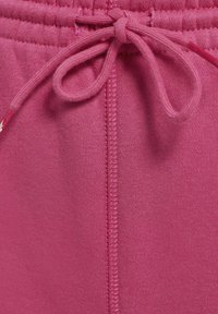 Różowe dresowe spodnie z bliska, z elastycznym paskiem ściągającym, gładką teksturą i widocznymi szwami.