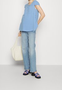 Světle modrý top s krátkým rukávem, volného střihu a detaily na stahování, v kombinaci s vybledlými modrými džíny a černými sandály na plošem podpatku se modrými popruhy.