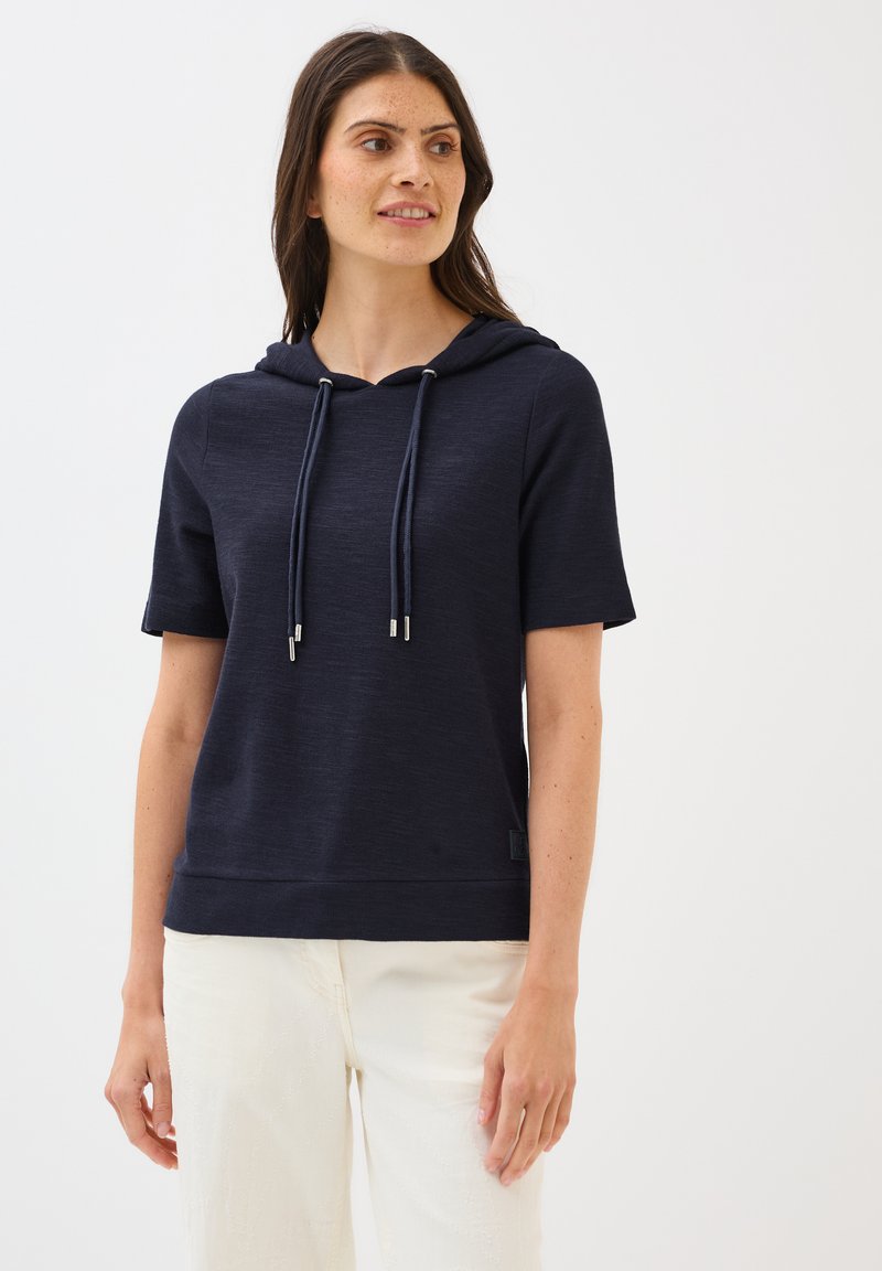 Short-sleeve navy hoodie made of soft fabric, featuring a drawstring, ribbed hem, and a small logo tag on the side.