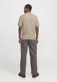 Suéter de punto beige de manga corta con un acabado texturizado, combinado con pantalones rectos grises y zapatos marrones. Vista desde la parte posterior.