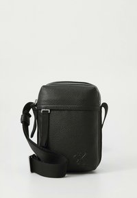 Svart texturerad läderväska med axelrem, dragkedja, justerbar rem och präglad logotyp på framsidan. Kompakt rektangulär form.