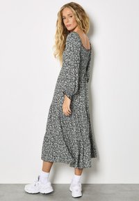 Vestido largo floral en blanco y negro con mangas abullonadas y escote en la espalda, combinado con zapatillas blancas y calcetines hasta el tobillo.