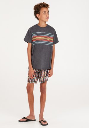 T-shirt grigia con righe orizzontali colorate; pantaloni da bagno a fantasia con disegni rettangolari multicolore; infradito nere.