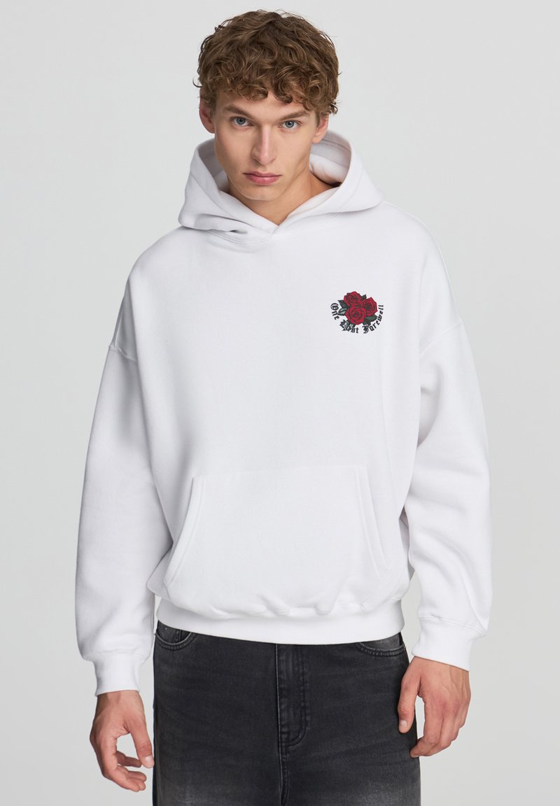 Felpa bianca con tasca frontale. Presenta un ricamo di una rosa rossa sul lato sinistro del petto. Tessuto morbido, vestibilità rilassata e cappuccio con coulisse.