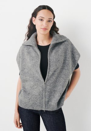 Gray zip-up vest made of soft fabric with a high collar and wide armholes, featuring ribbed hem details. Worn over a black top.