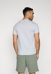 Gray short-sleeved t-shirt with a round neckline, featuring a small logo detail at the back. Paired with green shorts.