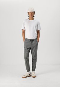 Grijze elastische taillebroek met trekkoord, witte crewneck t-shirt, beige pet en lichte sneakers. Eenvoudig ontwerp met een relaxte pasvorm.