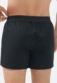 Svart simshorts med elastisk midja, med en slät tygtextur och en minimalistisk design, klippt ovanför knäet.