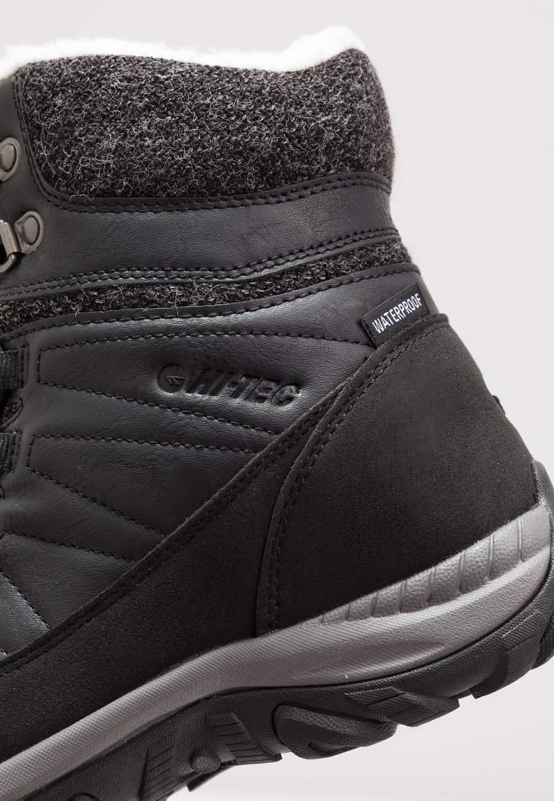 Botín negro impermeable con un cuello de tela texturizada gris, cuerpo de cuero liso y suela de goma gris con patrones de tracción.