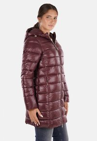 Giubbotto imbottito bordeaux con cappuccio, dotato di chiusura con zip frontale, design trapuntato, maniche lunghe e due tasche laterali con zip.