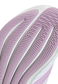 Suela de zapato con una superficie de goma morada con ranuras y crestas texturizadas, complementada por acentos en blanco y sutiles tonos verdes.