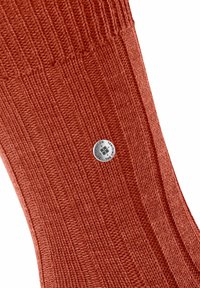 Pomarańczowa skarpetka z żebrowanym wzorem, wykonana z tkaniny plecionej, z metalicznym akcentem logo dla oznaczenia marki. Tekstura jest miękka i stworzona z myślą o komforcie.