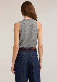 Szary top bez rękawów o fakturowanym wykończeniu, zestawiony z ciemnoniebieskimi, wysokim stanem dżinsami oraz błyszczącym brązowym paskiem z klamrą.