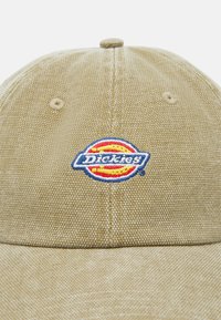 Kaki caps med textured stoff, en brodert logo med røde, gule og blå detaljer, samt et sydd ventilasjonshull.