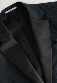 Blazer nero con un motivo strutturato blu, revers in satin e rivestimento interno liscio, con una finitura a contrasto lungo il colletto.