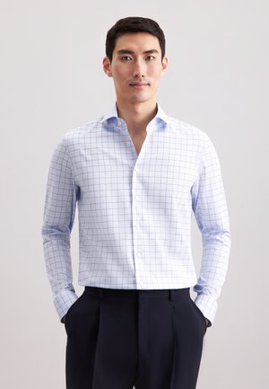 Camicia bianca con motivo a griglia blu, maniche lunghe e colletto a punta. Abbinata a pantaloni scuri. Tessuto dalla consistenza liscia.