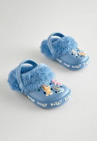 Blaue Clogs mit einem flauschigen, weichen blauen Futter, ausgestattet mit verspielten Charakteranhängern auf der Oberseite und einem weißen "Bluey"-Text an der Seite.