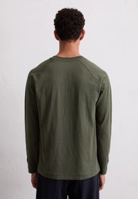 Langärmliges Shirt in Dunkelgrün, aus weichem Stoff. Mit geripptem Rundhalsausschnitt und Raglansärmel. Entspannt geschnitten, minimale Details.