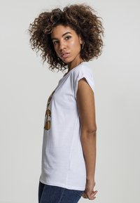 T-shirt en coton blanc avec des manches courtes retroussées et un graphique de dessin animé sur le devant. Associé à un jean en denim bleu foncé.