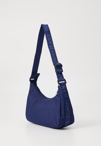 Sacoche bleu marine en nylon doux, de forme incurvée, avec fermeture éclair et une sangle ornée d'un logo en relief.