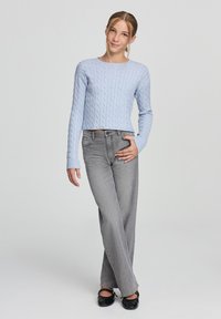 Maglione corto a costine di un blu chiaro, jeans dritti grigi e ballerine nere, caratterizzato da un design semplice con maniche lunghe e accenti a coste.