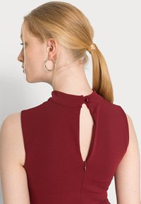 Vestido sem mangas em burgundy com gola alta, abertura nas costas com fecho de botão e fecho oculto na parte de trás. Textura suave.