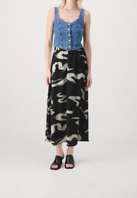 Cropped top in denim con bottoni e spalline larghe, abbinato a una lunga gonna nera con motivo astratto crema. Sandali neri con tacco a blocco e punta aperta.