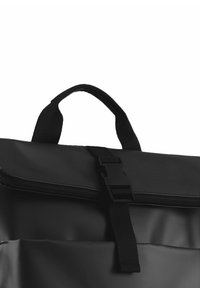 Mochila negra con una superficie texturizada, que cuenta con un asa en la parte superior, cierre de cremallera y una hebilla de plástico para un ajuste seguro.