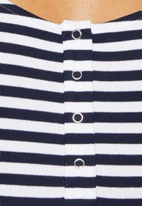 Top a righe in maglia blu navy e bianco, con righe orizzontali, una texture a costine e bottoni a pressione metallici sul retro del colletto.