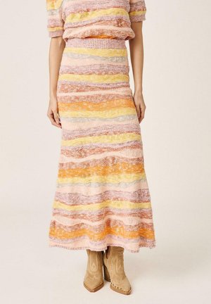 Mujer con un conjunto de falda y top de punto a rayas multicolores y botas de tobillo en tonos tierra, posando frente a un fondo liso.