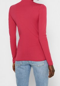 Langemouwen, aansluitend shirt van rode jersey stof met een hoge hals. Gecombineerd met lichtblauwe, relaxte denim jeans. Eenvoudig ontwerp, zonder patronen.