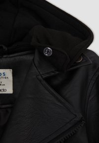 Veste en cuir noir avec une doublure en tissu noir doux, dotée d'un col boutonné, de coutures visibles et d'une étiquette de marque à l'intérieur.