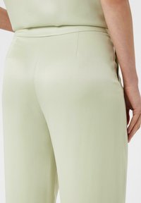 Jasnozielone satynowe spodnie o gładkiej fakturze, z dopasowanym pasem i dyskretnym detalem kieszeni z tyłu.